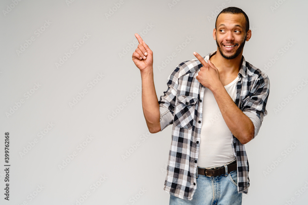 Joyful friendly african-american young man iwearing casual shirt pointing by finger at empty copy space Joyful friendly african-american young man iwearing casual shirt pointing by finger at empty copy space