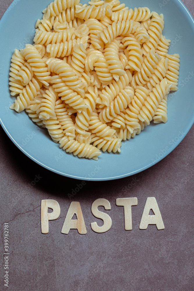 White fusilli pasta cooked and served on a blue plate on a grey background