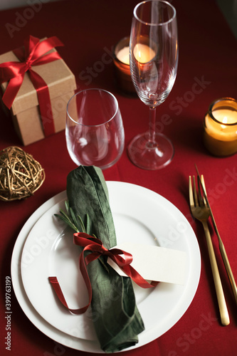Holiday table setting for one person on red tablecloth with gift box and candles. Christmas and Valentine's ideas, angle view.