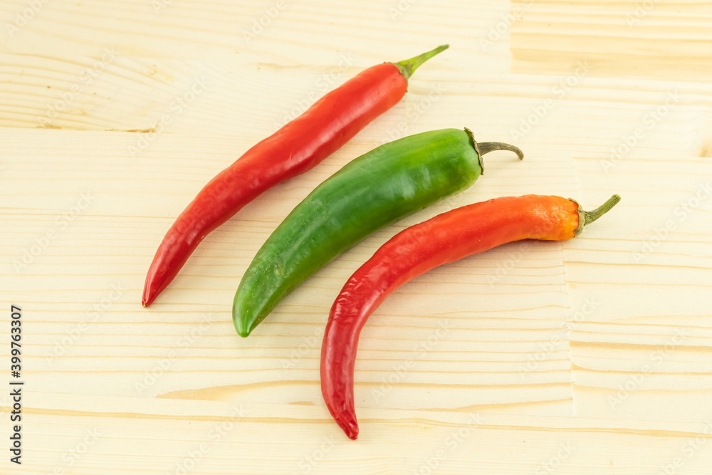 bright red chili peppers and green pod lie in parallel on a wooden background
