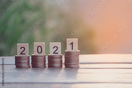 Text of 2021 number written on wooden blocks on top of coins stacks with nature sunset background, Business and Saving money for new life new year concept, Selective focus.