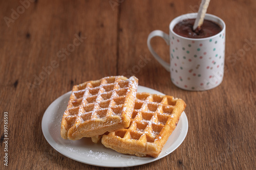 Two homemade waffles with a cup of hot chocolate over a wooden table.
