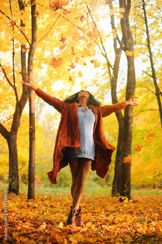 Young black woman throwing autumn leaves in the autumn forest