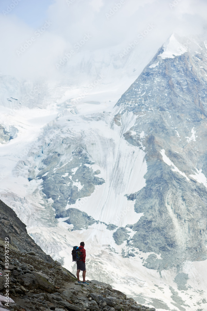 Vertical snapshot of incredibly beautiful mountain in Swiss Alps. Man tourist standing on a slope enjoying a cold quiete scenery. Concept of freedom, mountain hiking, tourism and alpinism