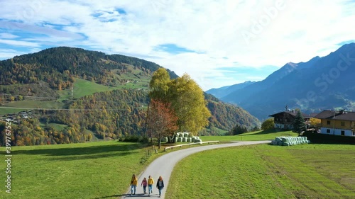 group of girls walking by the road between green fields at the austrian Alps at sunny autumn day
