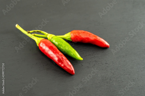 pair of mini chili peppers and green pod on a black background