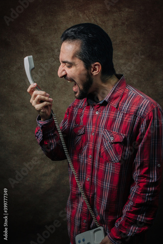Portrait of a man. The man shouts into the phone. Man in red plaid shirt