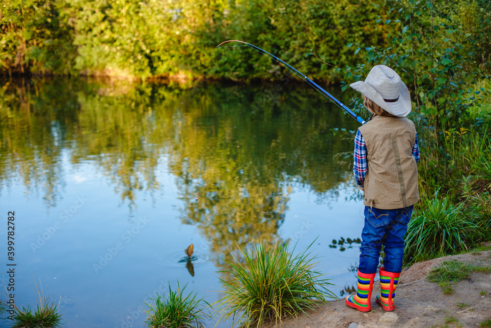 Child is fishing. Boy is a fisherman. Child with a fishing rod caught a  fish in a pond. Nice catch! Stock Photo