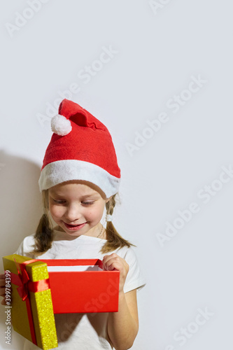 funny girl in a Santa claus hat opens a Christmas gift, portrait of a girl on a white background