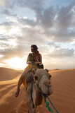 Asian woman riding a camel in Sahara Desert with the sunset at the background