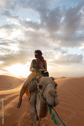 Canvas Print Asian woman riding a camel in Sahara Desert with the sunset at the background