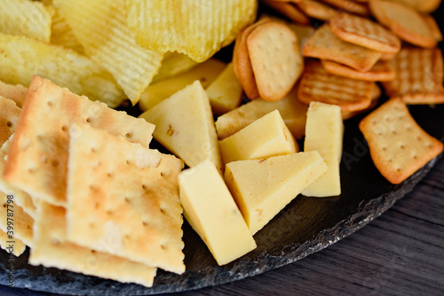 Mix of different snacks and appetizers. Street food plate with set of various kind snacks: bread spicy crackers, French fries and dip, tomatoes, delicious cheese on dark background. antipasto plate