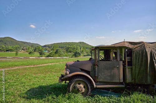 A military vehicle on a green meadow Behind it is a mountain and a clear blue sky with copy space.