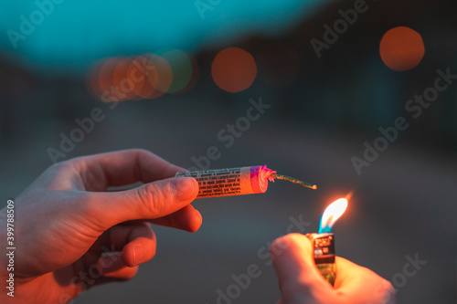 Young Man Lighting Up Firecracker in his Hand Outdoors in Evening. Guy Getting Ready for New Year Fun with Fireworks or Pyrotechnic Products - CloseUp Shot, Rear View