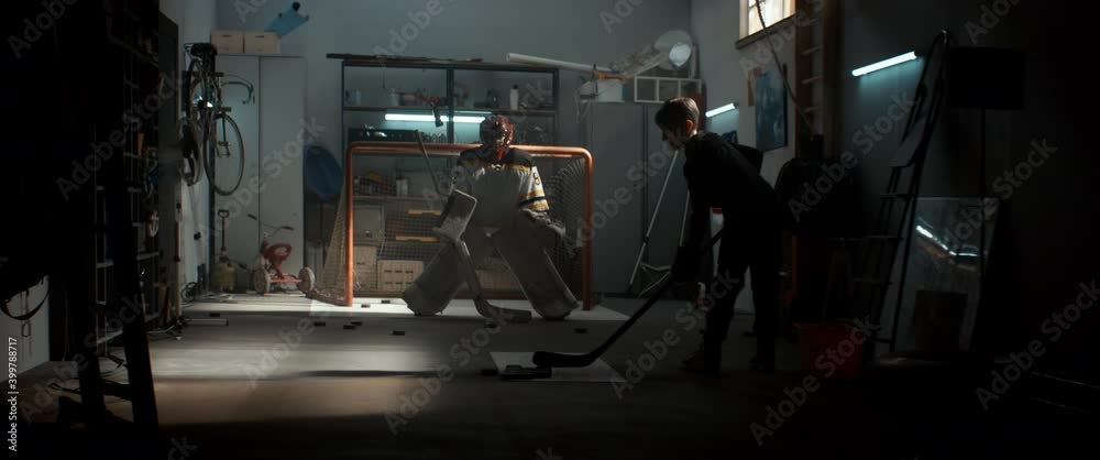 Kid boys friends or brothers practicing hockey shots inside a covered garage. Shot with 2x anamorphic lens Kid boys friends or brothers practicing hockey shots inside a covered garage. Shot with 2x anamorphic lens