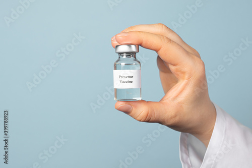 A doctor or laboratory technician keeps the Prevenar vaccine on a blue background. Vaccination against pneumocococy, prevention of pneumonia in infants photo