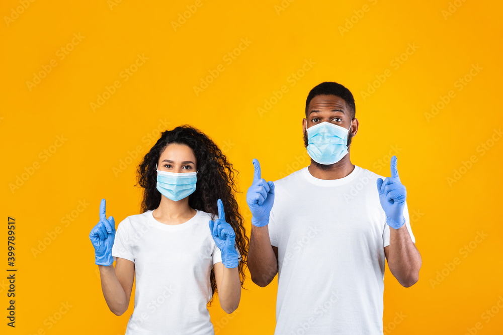 Couple Wearing Masks And Gloves Pointing Fingers Up, Yellow Background Couple Wearing Masks And Gloves Pointing Fingers Up, Yellow Background