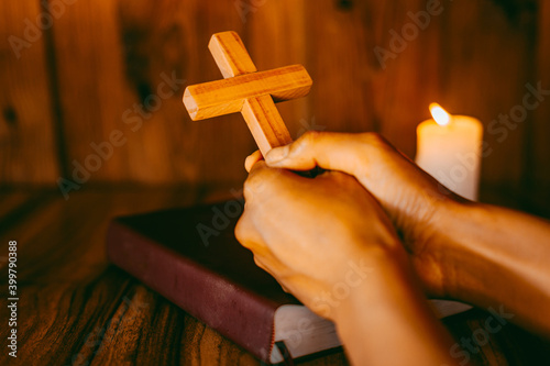 Hand holding the cross on the Bible and praying for the blessing of God with faith in His power, the idea of ​​faith in the divine power of God through prayer to Him, Christianity, Jesus.