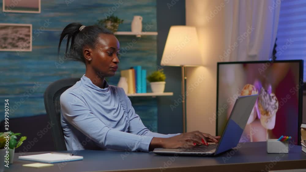 Tired black businesswoman working overtime reading projects sitting at desk in living room using laptop. Busy focused employee using modern technology network wireless overworking for job searching