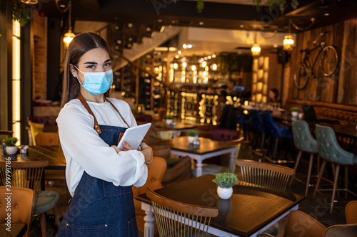 Waitress working on touchpad while wearing protective face mask. Beautiful waitress working at a restaurant wearing a facemask. Waitress wearing a facemask and using a tablet computer
