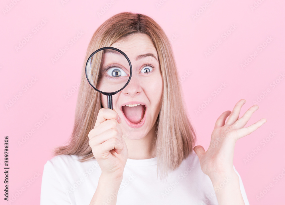 Young attractive blonde woman shocked while looking through a magnifying glass over pink background. Young attractive blonde woman shocked while looking through a magnifying glass over pink background.