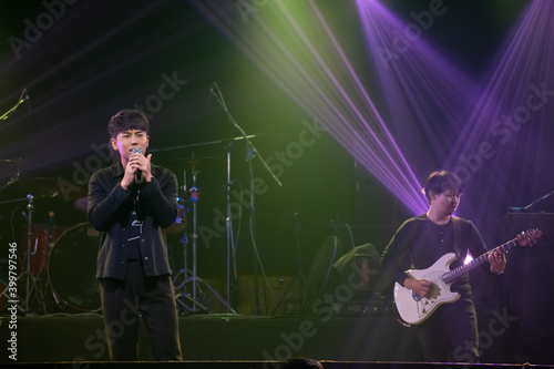 Asian singer and guitarist of rock band musicians perform in concert on stage