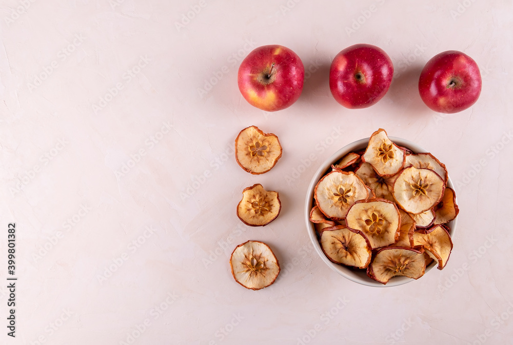 A bowl of dried apple pieces and a few ripe red apples on a light surface. The concept of useful products. Selective focus, copy space, wiew from above. A bowl of dried apple pieces and a few ripe red apples on a light surface. The concept of useful products. Selective focus, copy space, wiew from above.