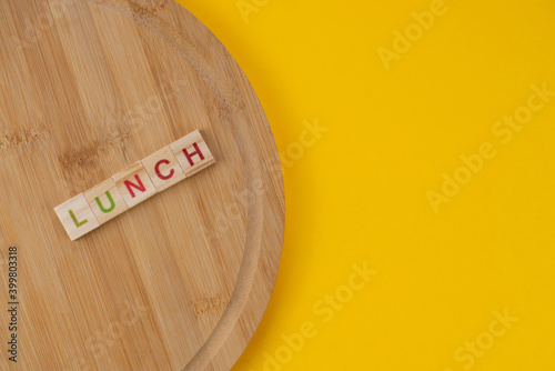 Lunch menu concept. Scrabble letter tiles on wooden table. Yellow background.