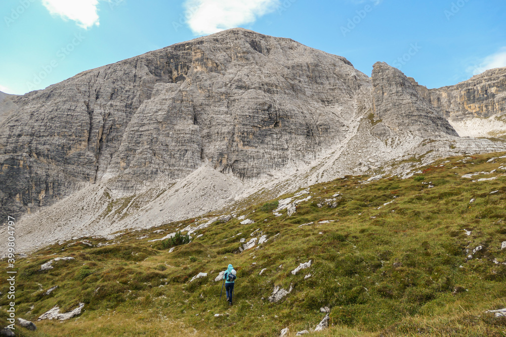 A woman hiking in a high and desolated mountains in Italian Dolomites. The lower parts of the mountains are overgrown with moss and grass. Raw and unspoiled landscape. Clear and sunny day. Solitude