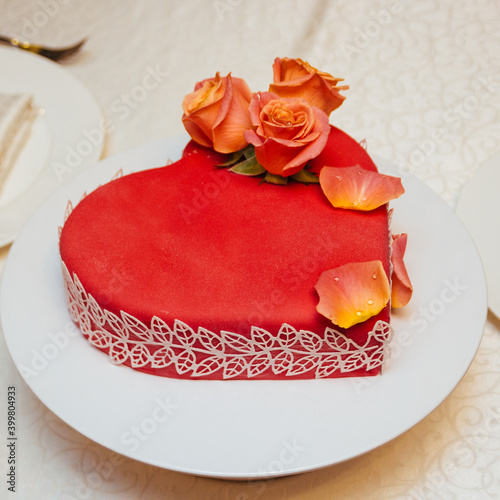 Red heart-shaped cake decorated with vibrant live roses on a festive table.