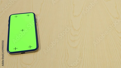 Digital Smartphone on wood desk with blank green screen. Close-up of mobile phone sliding on table for presentation. 3d render animation of cellphone device on background with chroma key display.
