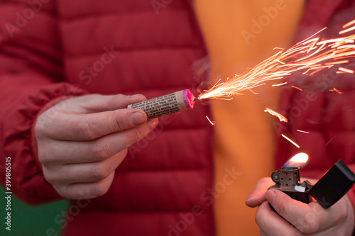 Man in Red Jacked Lighting Up Firecracker in his Hand Using Gasoline Lighter. Guy Getting Ready for New Year Fun with Fireworks or Pyrotechnic Products