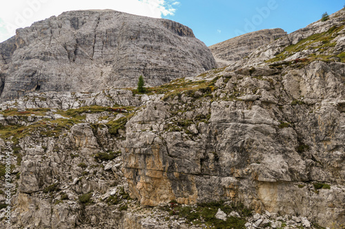 A close up view on a massive, high and desolated mountain wall in Italian Dolomites. The wall has sandy color with some darker shades. Dangerous climbing route. Few green plants on the steep slopes. © Chris