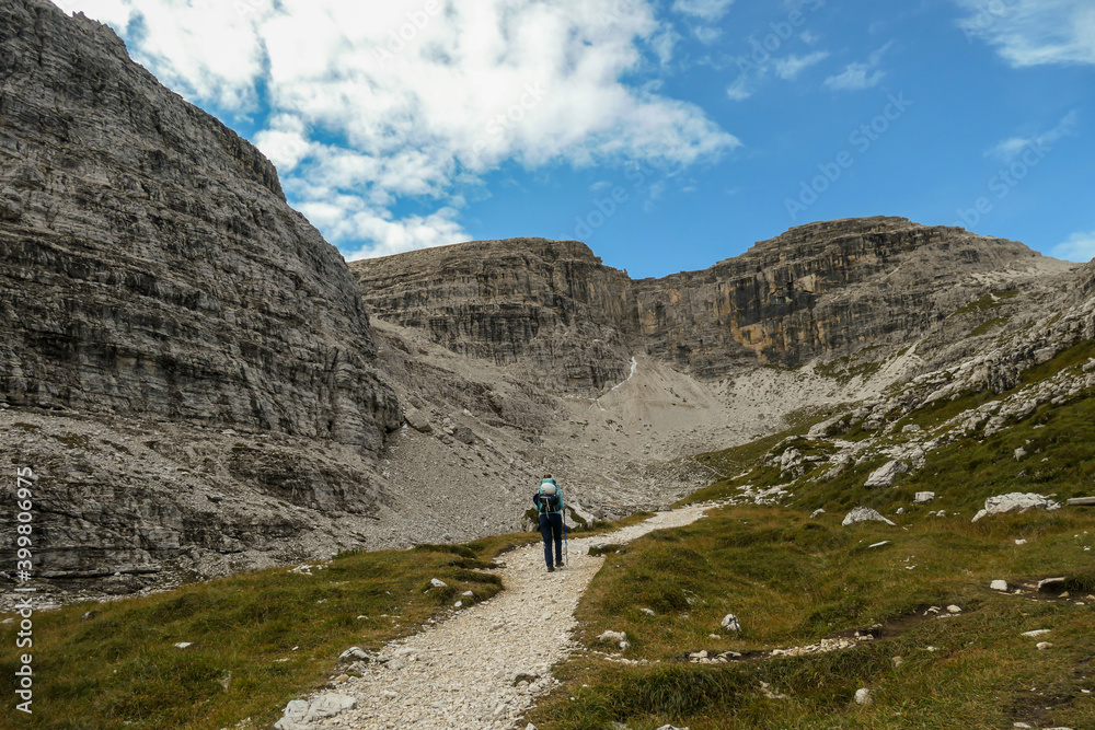A woman hiking in a high and desolated mountains in Italian Dolomites. The lower parts of the mountains are overgrown with moss and grass. Raw and unspoiled landscape. Clear and sunny day. Solitude