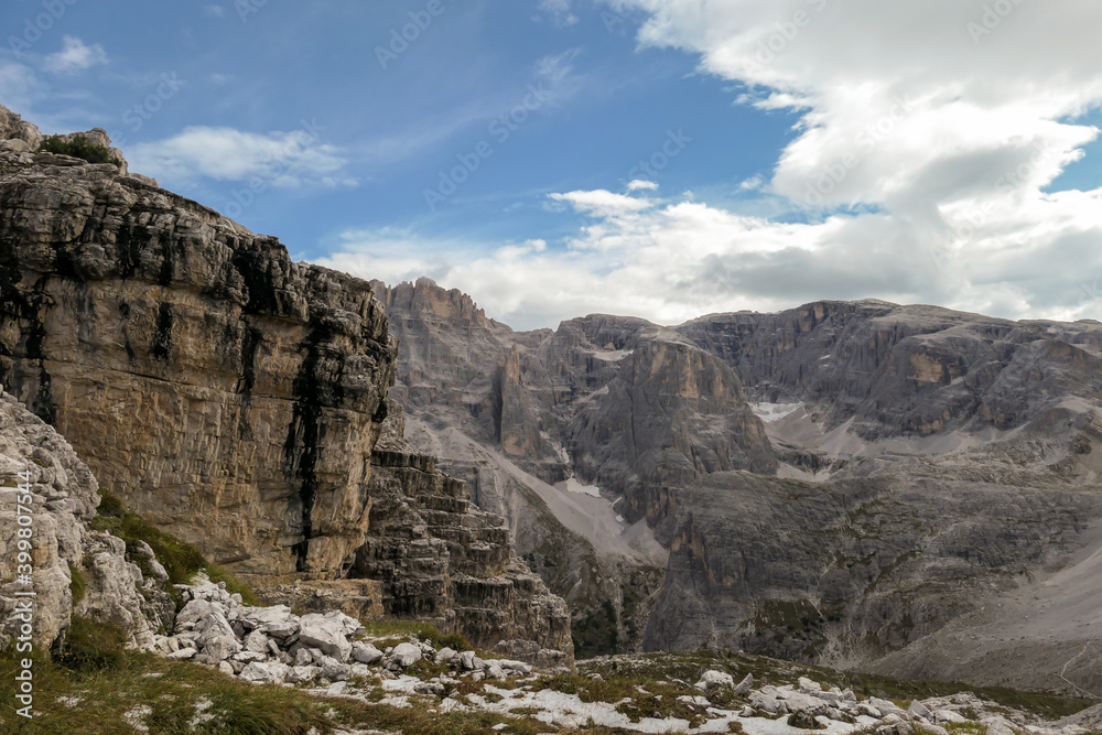 Panoramic view on the valley in Italian Dolomites. The bottom of the valley is overgrown with small plants. In the back there is a high mountain chain, with very sharp slopes. Serenity and recharging