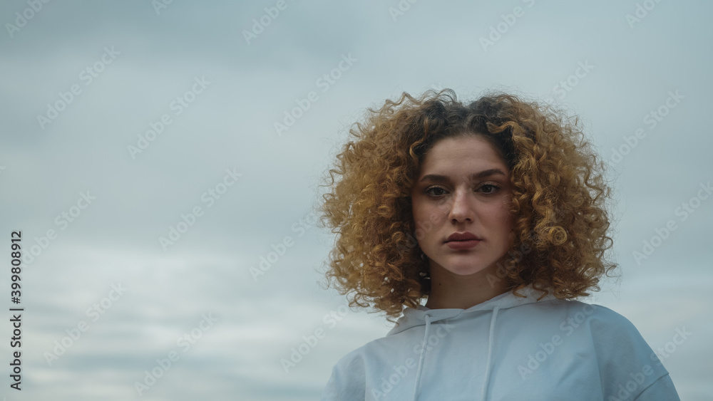 Portrait of young woman in white sportswear with curly hair. Cloudy weather background Portrait of young woman in white sportswear with curly hair. Cloudy weather background