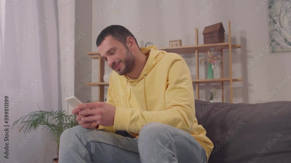 happy hispanic man texting on smartphone and smiling in living room happy hispanic man texting on smartphone and smiling in living room