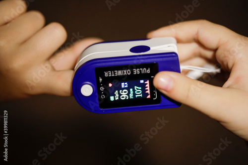 Details with the hands of a little girl measuring her pulse and blood oxygen level with a self use pulse oximeter at home during the Covid-19 outbreak.
