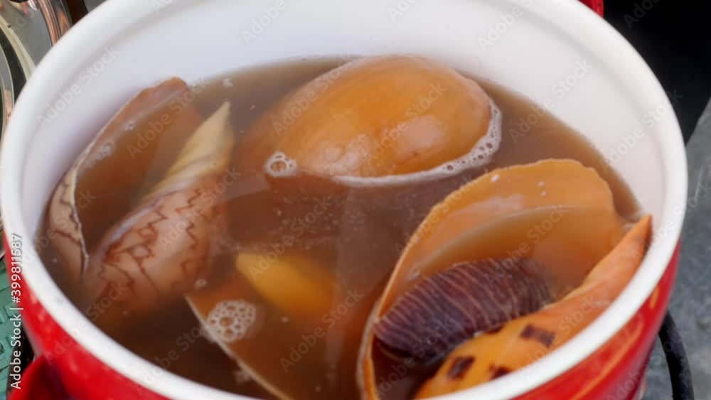 Woman hand opens the lid at the red pan with boiled Giant Sea Snail Woman hand opens the lid at the red pan with boiled Giant Sea Snail