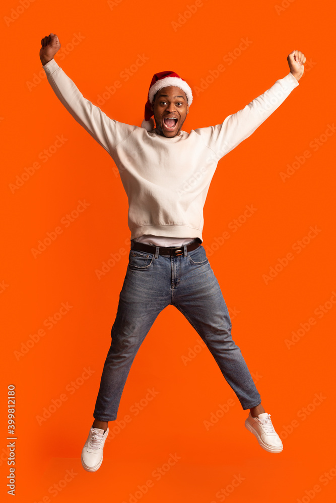Portrait Of Funny Black Guy In Santa Hat Jumping With Raised Hands Portrait Of Funny Black Guy In Santa Hat Jumping With Raised Hands