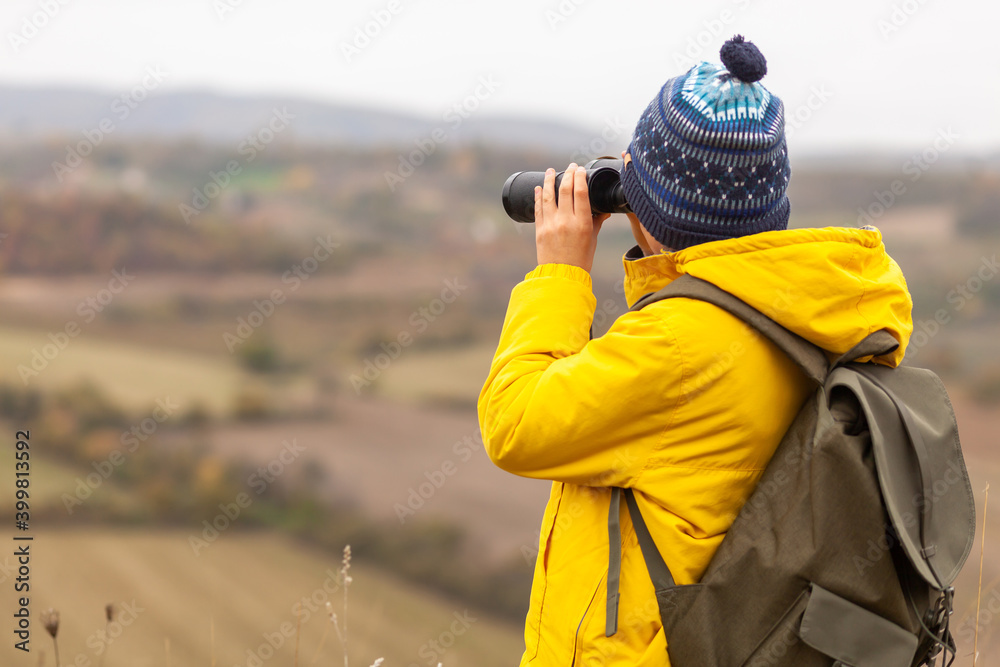 Obraz premium Rear view of a little boy looking through binoculars during autumn day from a hill.