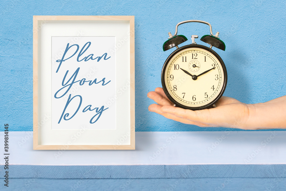 Hand holding an alarm clock next to a wooden frame with the sentence