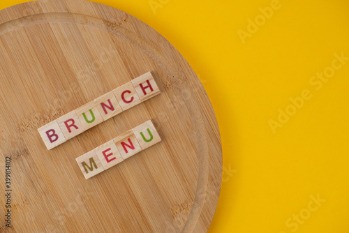 Brunch menu concept. Scrabble letter tiles on wooden table. Yellow background.