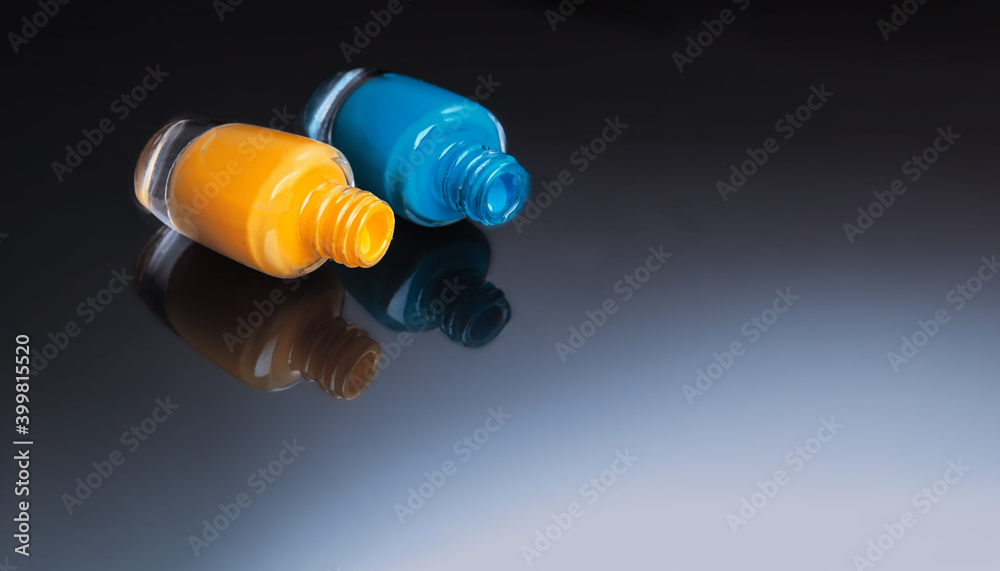 Two of multicolored bottles of nail polish with reflections in a mirror surface on a dark background Two of multicolored bottles of nail polish with reflections in a mirror surface on a dark background