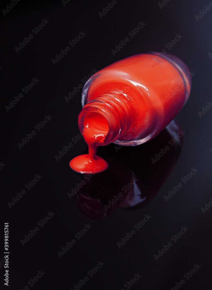 Side view of one red bottle of nail polish with reflections on mirrored surface against dark background Side view of one red bottle of nail polish with reflections on mirrored surface against dark background