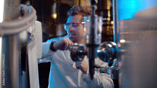 Portrait of happy scientist in white coat and goggles dancing in large industrial laboratory