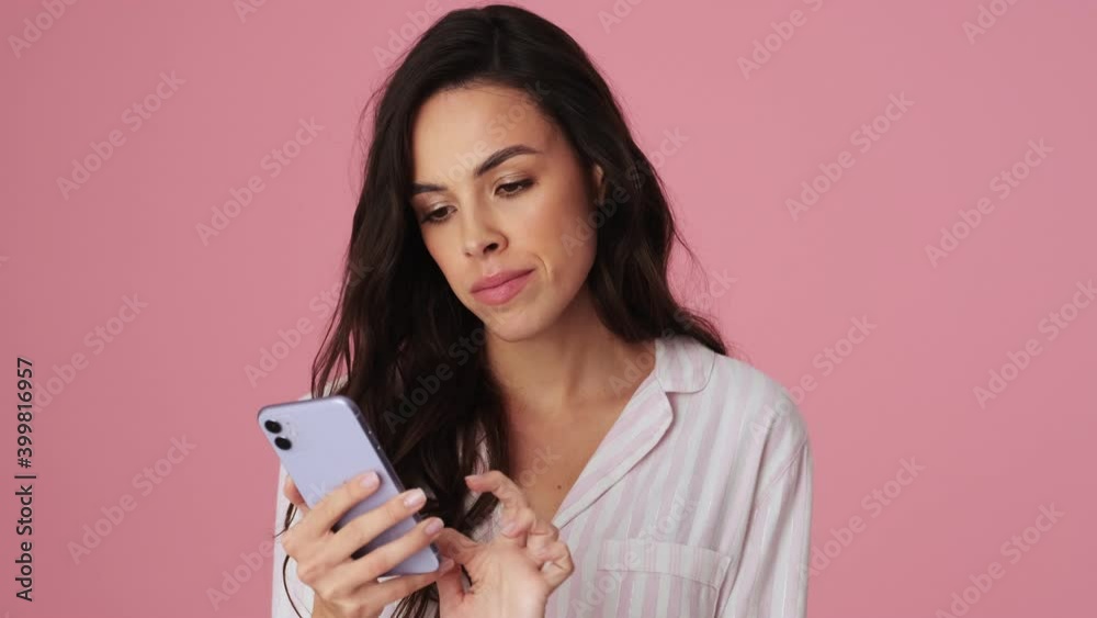 A happy young woman is using her smartphone and standing isolated over a pink background in the studio A happy young woman is using her smartphone and standing isolated over a pink background in the studio
