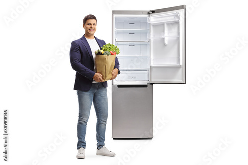 Full length portrait of a young man with a grocery bag and a fridge photo