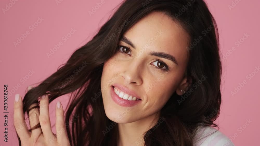 A close-up view of a charming young woman is posing to the camera standing isolated over a pink background in the studio A close-up view of a charming young woman is posing to the camera standing isolated over a pink background in the studio