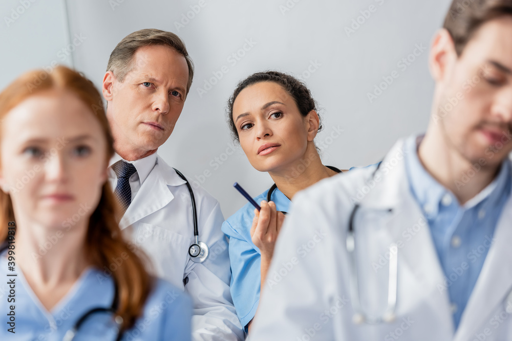 Concentrated multicultural colleagues looking away during meeting on blurred foreground in hospital Concentrated multicultural colleagues looking away during meeting on blurred foreground in hospital
